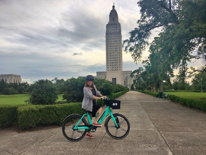 This is a picture of the Louisiana State capitol with a woman on a bike.